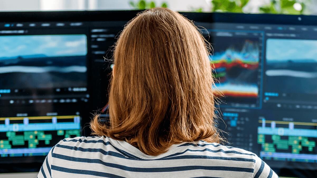 a video editor stares at an editing timeline and color waveform on dual computer screens